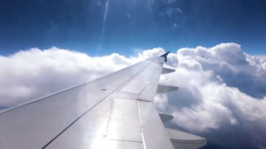 Uçak kanadı ve mavi gökyüzü, uçuş sırasında beyaz bulutlar...
