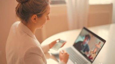 Evde cep telefonu ve defter üzerinde çalışan bir kadın, online konferans
