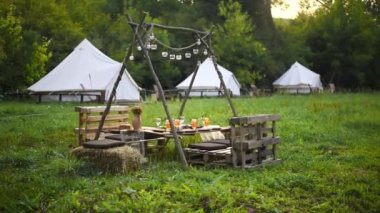 Table with food and drinks at glamping, Greenery around, tents on the background