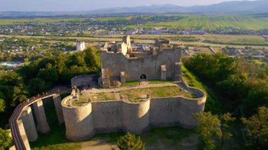 Romanya 'nın Targu Neamt kentindeki Neamt Kalesi' nin insansız hava aracı görüntüsü. Tepenin tepesinde turistlerle dolu bir kale. Etrafı yemyeşil ormanlarla çevrili. Arka planda kasaba.