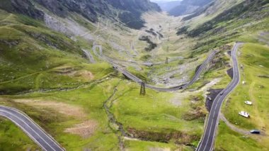 Aerial drone view of nature in Romania. Transfagarasan route in Carpathian mountains with moving cars, rocky slopes with greenery