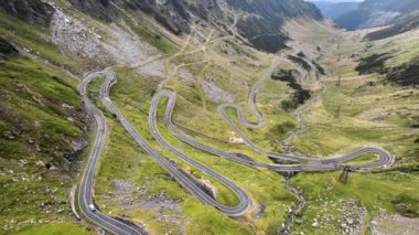 Aerial drone view of nature in Romania. Transfagarasan route in Carpathian mountains with moving cars, rocky slopes with greenery