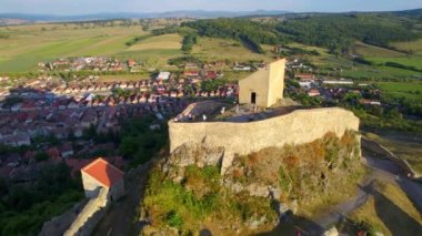 Aerial drone view of Rupea Fortress at sunset, Romania. Citadel located on a cliff, tourists, town, greenery