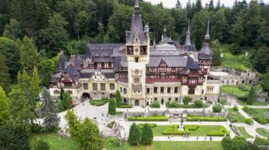 SINAIA, ROMANIA - AĞUSTOS, 2022: Romanya 'daki Peles Kalesi' nin insansız hava aracı görüntüsü. Karpatlar 'da bahçeleri ve turistleri olan bir kale. Etrafında bereketli ormanlar var.