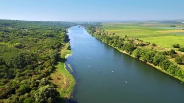 Moldova 'daki Dinyester' da raket sörfü yapan birden fazla insanın insansız hava aracı görüntüsü. Nehrin iki yakasındaki yemyeşil orman, tarlalar ve bir köy.