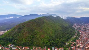 Aerial drone view of Brasov, Romania. Old city with traditional buildings, hill with lush greenery and city sign on top of it