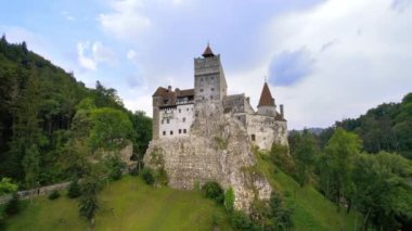 Romanya 'daki Bran Kalesi' nin insansız hava aracı görüntüsü. Karpatlar 'daki ortaçağ şatosu, etrafta yeşil ağaçlar, yürüyen turistler.