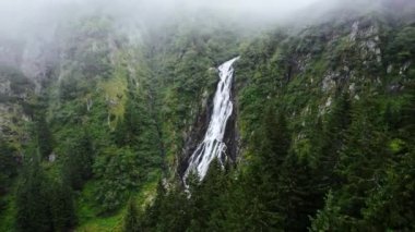Aerial drone view of nature in Romania. Carpathian mountains with waterfall and tourists, rocky slopes with greenery, fog