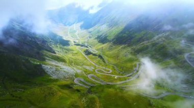 Aerial drone view of nature in Romania. Transfagarasan route in Carpathian mountains with moving cars visible through clouds, rocky slopes with greenery