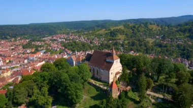 Romanya 'nın Sighisoara Tarih Merkezi' nin insansız hava aracı görüntüsü. Eski binalar, tepedeki kilise, yeşilliklerle çevrili.