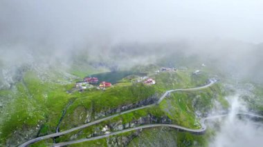 Romanya 'da doğanın insansız hava aracı görüntüsü. Karpatya dağlarındaki transfagarasan rotası, Balea Gölü tatil beldesi bulutların arasından görünen, yeşil yamaçlarla kaplı kayalık yamaçlar.