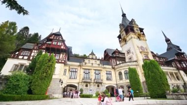SINAIA, ROMANIA - 2022 AĞUSTOS: Peles Kalesi manzarası. Karpatlar 'da bahçeleri ve önünde turistleri olan bir kale.