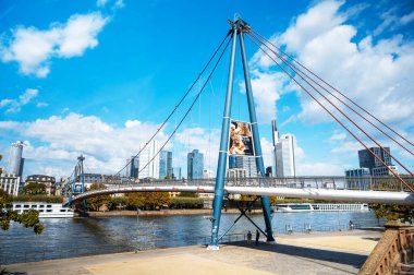 FRANKFURT, ALMANY - Eylül 2022: Şehir manzarası. Nehir kıyısındaki köprü, yeşillik, insanlar, binalar ve gökdelenler