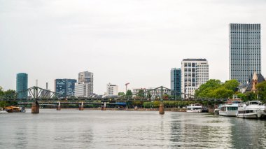 Frankfurt şehri, Almanya 'da. Köprüsü, demirlemiş tekneleri, modern binaları ve arka planında gökdelenleri olan River Main.