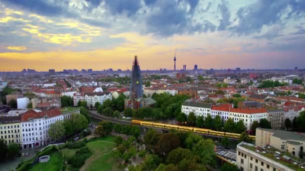 ドイツの日没時にベルリンのクロイツベルクの空中ドローンビュー 緑と住宅地 建物やベルリンテレビ塔の距離で 列車を移動 — ストック動画