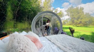 Bir çift glamping 'de şeffaf bir kabarcık çadırına girip sohbet ediyorlar, içeriden görüyorlar. Çevredeki yemyeşil orman