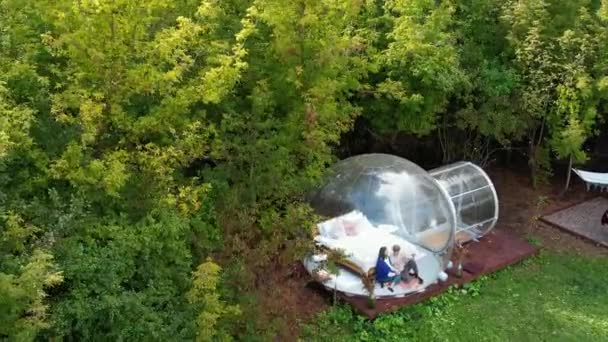 Tenda Bolha Transparente Glamping Floresta Exuberante Redor Interior Casal Sentado — Vídeo de Stock