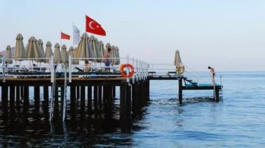 KEMER, TURKEY - 2022 EYLÜL: günbatımında Akdeniz kıyısı sahili görüntüsü. Rıhtımda dinlenen insanlar