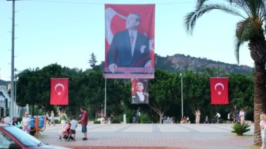 KEMER, TURKEY - Eylül 2022: günbatımında merkez meydanı manzarası. Mustafa Kemal Atatürk 'ün portresi olan ulusal bayrak, yürüyen insanlar, yeşillik