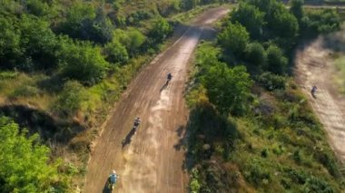 Motosikletlilerin hava aracı görüntüsü bir motokros yarışında sıçrama tahtalarından, çamur pistinden, rali motorsikletlerinden, yeşillikten atlıyor.