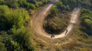 Motosikletlilerin hava aracı görüntüsü bir motokros yarışında sıçrama tahtalarından, çamur pistinden, rali motorsikletlerinden, yeşillikten atlıyor.