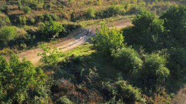 Motosikletlilerin bir motokros yarışında sıçrama tahtalarından, çamur pistinden, rali motorsikletlerinden, yeşillikten atlayışını gösteren hava aracı görüntüsü. Yavaş çekim