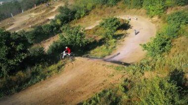 Motokros, çamur pisti, rali motosikletleri, yeşillik çevresindeki sıçrama tahtasından atlayan motorcuların insansız hava aracı görüntüsü. Yavaş çekim