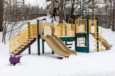 Parktaki slaytlı oyun alanı yapısı çocuksuz, kış mevsiminde karla kaplı.