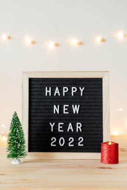 Mutlu yıllar 2022 siyah keçeli mektup tahtası ve küçük Noel ağacı ve ahşap masada mum üzerine yazılmış.