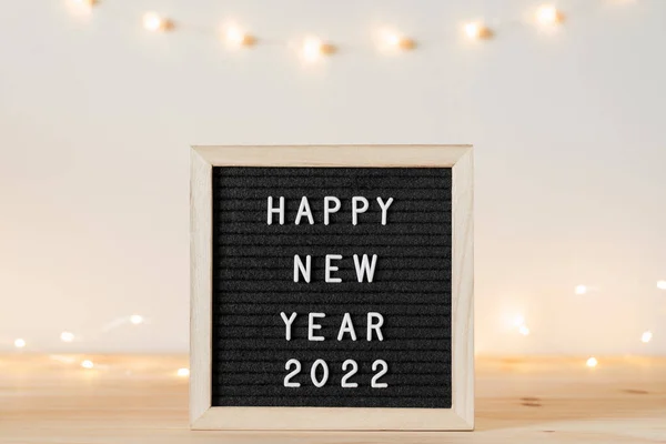 Feliz año nuevo 2022 saludos en el tablero de cartas en la mesa de madera con luces de fiesta —  Fotos de Stock