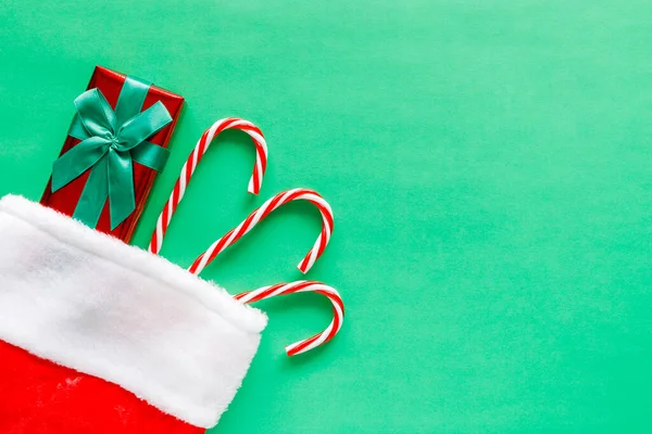 Christmas stocking with present and candy canes on green background. — Stock Photo, Image