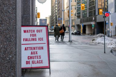 Kaldırımdaki tabela buz ve kar tehlikesi uyarısı yapıyor.