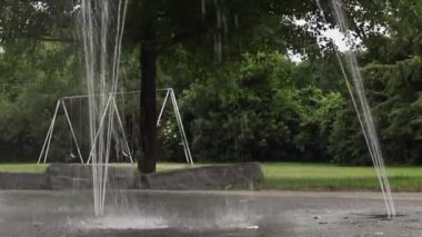 Halka açık bir parkta su sıçratma yastığı ve salıncaklar.
