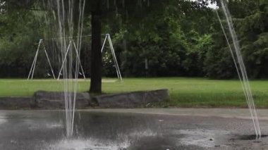Halka açık bir parkta su sıçratma yastığı ve salıncaklar.