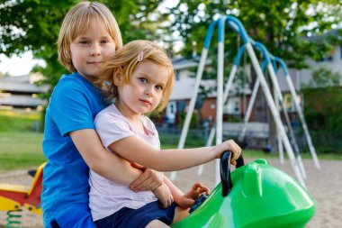 Yazın parkta çocuklar. Erkek kardeş kız kardeşe sarılıyor. Kardeşler oyun alanında birlikte oynuyorlar. Aile etkinliği