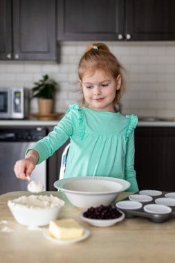 Ev yapımı kek pişirmek için malzemeleri karıştıran gülümseyen küçük kız. Çocuk evde mutfakta yemek pişiriyor. Çocuk para kazanıyor.