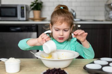 Küçük kız mutfakta para kazanıyor. Küçük çocuklar yemek yapıyor. Çocuk ev yapımı kekler yapıyor, hamur işleri için malzemeleri karıştırıyor..
