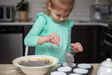 Küçük kız evde mutfakta ev yapımı kek yapıyor. Küçük çocuk kek pişiriyor. Çocuk pişirme