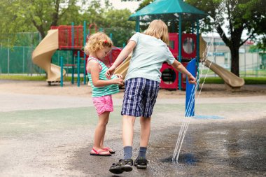 Küçük mutlu çocuklar sıcak yaz gününde parkta su sıçratma havuzunda oynuyorlar. Çocuklar yazın dışarıda eğleniyor..