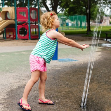 Küçük mutlu çocuk sıcak yaz gününde parkta su sıçratma havuzunda oynuyor..