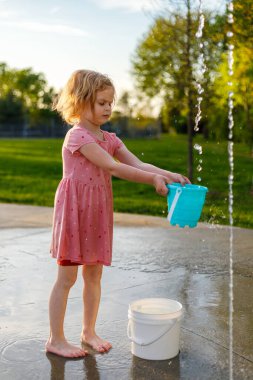 Küçük çocuk sıcak bir yaz gününde parkta su sıçratma yerindeki oyun parkında suyla oynuyor.