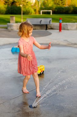 Küçük kız yazın fıskiyelerle parkta oynuyor. Küçük çocuk yazın su sıçratma parkında eğleniyor.