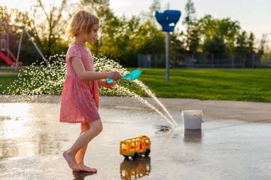 Küçük çocuk yazın su sıçratma parkında açık hava oyuncaklarıyla oynuyor. Çocuklar için çeşmeleri olan bir su parkı. Çocuklar için yaz etkinlikleri