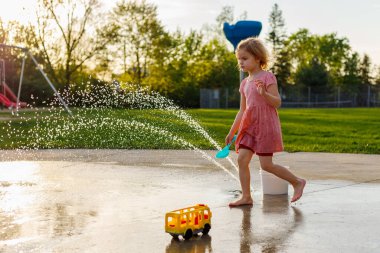 Küçük bir çocuk yazın su sıçratma parkında oynuyor. Çocuklar için çeşmeleri olan bir su parkı. Çocuklar için yaz etkinlikleri
