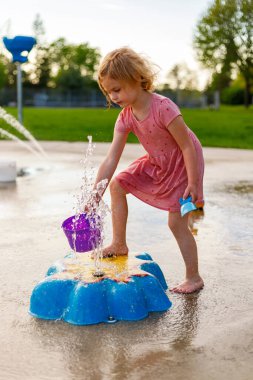 Küçük çocuk yazın parkta su sıçratma yerindeki çocuk parkında oyuncaklarıyla oynuyor. Çeşmelerin yanındaki küçük çocuk akşamları dışarıda vakit geçiriyor.