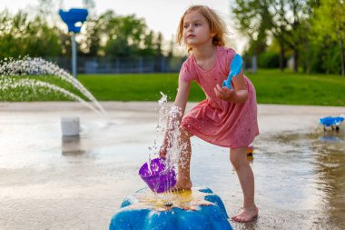 Küçük bir çocuk yazın su sıçratma parkında oynuyor. Çocuklar için çeşmeleri olan bir su parkı. Çocuklar için yaz etkinlikleri