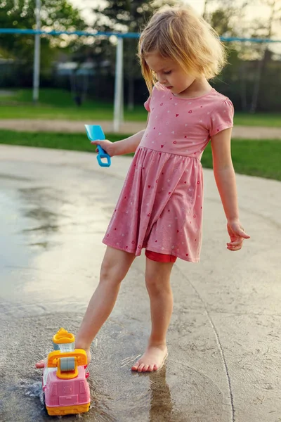 Small child playing at splash pad with water and outdoor toys. Little girl having fun at playground with fountains in summer.