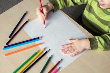 Masada beyaz kağıda renkli kalemler çizen küçük bir çocuk. Üst görünüm.