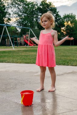 Su parkında duran küçük kız. Yazın açık havada çeşmenin yanında oynayan çocuk.
