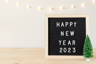 Siyah keçeli mektup panosundaki yeni yılınız kutlu olsun. Masadaki küçük Noel ağacı ve beyaz duvardaki tatil ışıkları. Metin için alanı kopyala